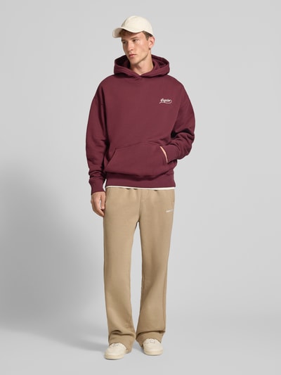 Männermodel trägt Loose Fit Sweatpants aus Baumwoll-Mix mit Label-Detail von PEGADOR in Beige, kombiniert mit Kapuzenpullover, Kontext: Herren Sweatpants, Baumwoll-Mix, Loose Fit, Label-Detail, Eingrifftaschen, elastischer Bund, Innenbeinlänge 70 cm bei Größe M, Ganzkörperansicht von vorne.