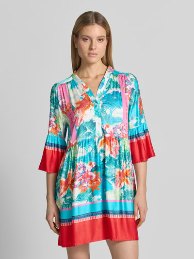 Frauenmodel trägt Relaxed Fit Minikleid aus reiner Viskose Modell 'Breeze' von miss goodlife mit floraler Allover-Print, Halbarm, V-Ausschnitt, Knopfleiste und Falten-Optik in leuchtenden Blau-, Rot- und Pinktönen, Ganzkörperansicht von vorne. Rückenlänge 40 cm, Brustweite 39 cm, Ärmellänge 46 cm.