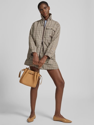 Frauenmodel trägt Bucket-Bag mit Logo-Detail von Tory Burch in Camel, Hauptfach mit Zugband, abnehmbarer Schulterriemen, kurzer Tragehenkel, Breite 22 cm, Länge 22 cm, Tiefe 11 cm, Ganzkörperansicht von vorne.