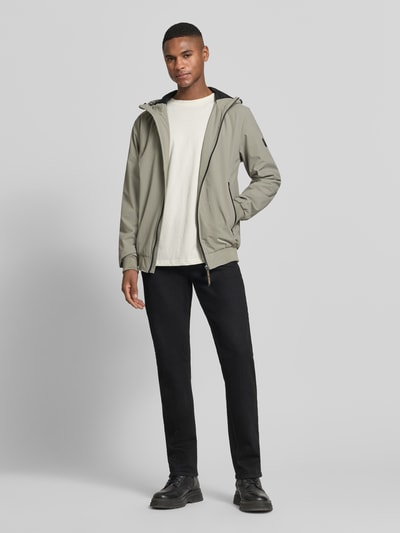 Męskimodel nosi kurtkę z kapturem w kolorze oliwkowym, model 'MATTEO' od CARS JEANS, mieszanka materiałów z dodatkiem streczu, krój regular fit, zamek błyskawiczny, kieszenie zapinane na zamek błyskawiczny, długość tyłu w rozmiarze M: 70 cm, szerokość ramion w rozmiarze M: 44 cm, szerokość klatki piersiowej w rozmiarze M: 50 cm, długość rękawów w rozmiarze M: 70 cm, widok całej sylwetki z przodu.