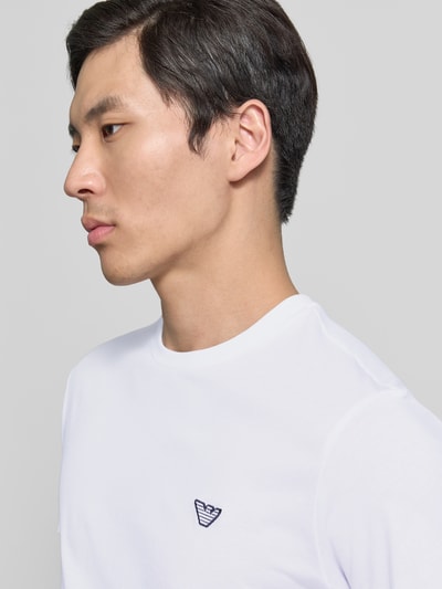 Männermodel trägt T-Shirt mit Logo-Patch und Rundhalsausschnitt von Emporio Armani in Weiß aus Reine Baumwolle, Modern Fit, Nahaufnahme Oberkörper. Rückenlänge Größe M: 69 cm.