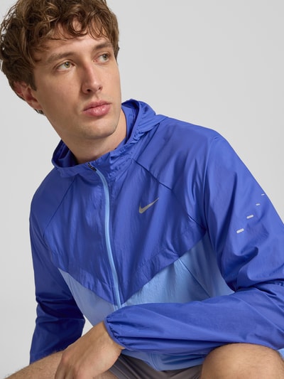 Männermodel trägt Trainingsjacke mit Logo-Print und Kapuze von NIKE TRAINING in Blau, Reißverschluss, Nahaufnahme Oberkörper.