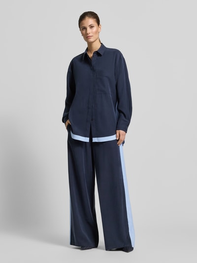 Vrouwenmodel draagt 'Fließende Viskose-Bluse mit Kontraststreifen - curated by Tinvcb' van SIC, losse fit, overhemdkraag, verborgen knoopsluiting, borstzak, marineblauw met lichte strook, lengte 80 cm, mouwlengte 58 cm, geheel van voren bekeken.