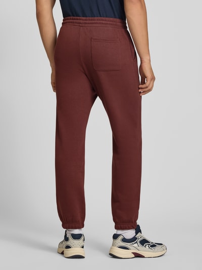 Männermodel trägt Straight Fit Sweatpants aus Baumwoll-Mix Modell 'Kane' von JACK & JONES in Rotbraun, Gesäßtasche, Rückansicht, Ganzkörperansicht von hinten.