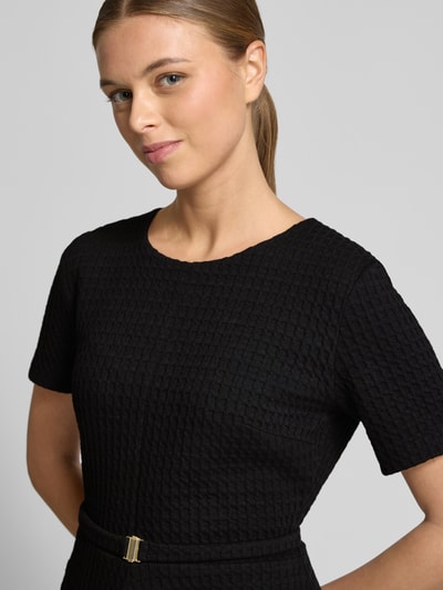 Vrouwenmodel draagt knielangens jurk uit katoenmix met structuurpatroon van Marc Cain, getailleerde pasvorm, ronde hals, korte mouw, logodetail, afneembare stoffen riem, elastische katoenmix. Nahaufnahme bovenlichaam.