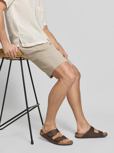 Männermodel trägt Shorts mit elastischem Bund und Eingrifftaschen von MCNEAL in Beige mit Strukturmuster, Regular-Fit, Nahaufnahme Oberschenkel von vorne. Kontext: Herren Shorts mit Gesäßtaschen, Tunnelzug, Bundweite 44 cm, Innenbeinlänge 26 cm, Größe M.