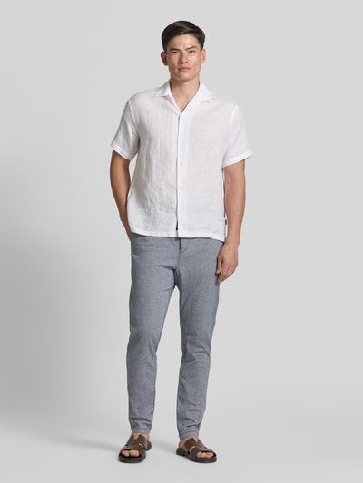 Męski model nosi Regular Fit Chino aus Baumwoll-Mix von Tom Tailor w melanżowej szarości, bawełniany materiał, krój regular fit, label patch, szlufki, tunel na pasek, kieszenie tylne i boczne, zapięcie na guzik i zamek, widok całej sylwetki z przodu.