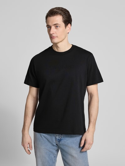 Männermodel trägt T-Shirt mit Rundhalsausschnitt von CK Calvin Klein, schwarze Farbe, Regular-Fit, Logo, Reine Baumwolle, Ganzkörperansicht von vorne. Rückenlänge bei Größe M: 67 cm.