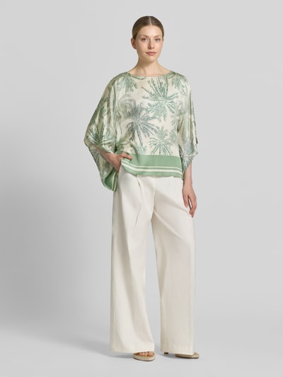 Frauenmodel trägt Relaxed Fit Kurzarmbluse aus reiner Viskose von s.Oliver BLACK LABEL mit Palmenprint in Grün und Creme, fließende Textur, Ganzkörperansicht von vorne.