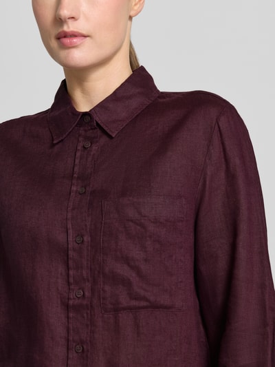 Frauenmodel trägt Leinenbluse mit Brusttasche Modell 'LINO' von Mango in dunklem Bordeaux, reine Leinen, Kentkragen, Loose-Fit-Modell, Knopfleiste, Sportmanschetten, Ganzkörperansicht von vorne.