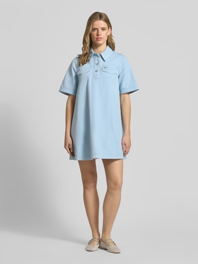 Frauenmodel trägt Oversized Minikleid aus reiner Baumwolle von Tommy Jeans in Optik: Unifarben, Passform: Oversize, Länge: Mini, Ausschnitt: Hochgeschlossen, Applikation: Logo-Stitching, Verschluss: Knopfleiste, Ärmelform: Kurzarm, Material: Reine Baumwolle; Ganzkörperansicht von vorne.