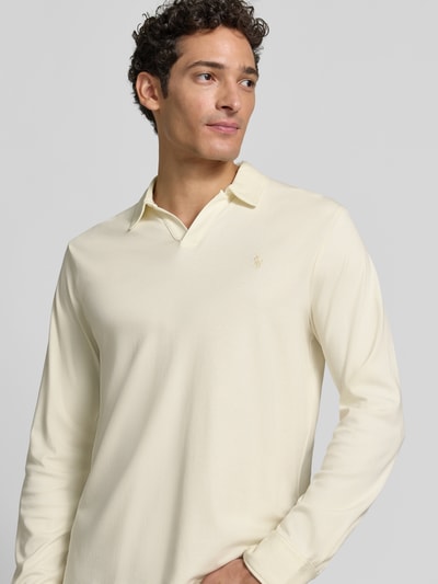 Männermodel trägt Slim Fit Poloshirt aus reiner Baumwolle von Polo Ralph Lauren in hellem Creme, dezente Textur, Nahaufnahme Oberkörper.