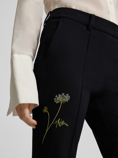 Frauenmodel trägt schwarze Stoffhose mit grüner Blumenstickerei, französische Eingrifftaschen, Modell 'FRANCOISE' von Cambio, Nahaufnahme Oberkörper, Viskose-Mix mit Stretch-Anteil.