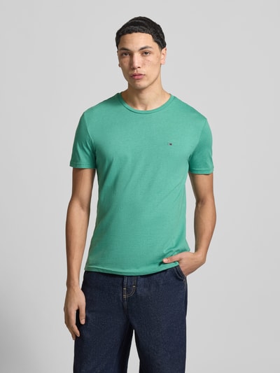 Männermodel trägt Slim Fit T-Shirt aus Baumwoll-Mix Modell 'JASPE HERITAGE' von Tommy Jeans in Melange-Optik, Logo-Stitching, Kurzarm, Ganzkörperansicht von vorne.