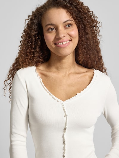 Vrouwenmodel draagt Slim Fit langarmshirt uit katoenmix model 'LAILA' van Only, unikleuren, fijnrib, muschelrand, cropped, geknoopt, close-up bovenlichaam.