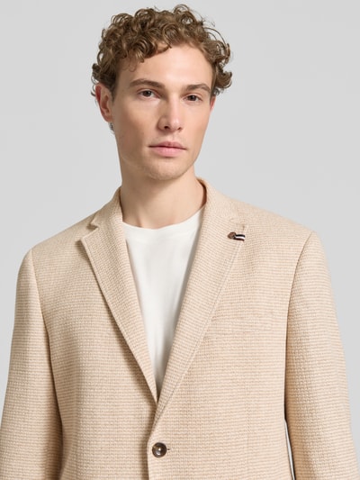 Męski model nosi Slim Fit 2-Knopf-Sakko mit Strukturmuster von bugatti w beżowym kolorze, mieszanka bawełny, kołnierz z połami, nakładane kieszenie, długość tyłu 73 cm, szerokość ramion 48 cm, długość rękawów 65 cm, fakturowany wzór, krój slim fit, półzbliżenie górnej części ciała z przodu.