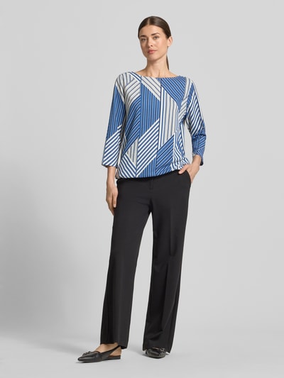 Frauenmodel trägt Regular Fit Blusentop mit Allover-Muster von s.Oliver RED LABEL, Optik:Allover-Muster, Passform: Regular-Fit, Kragenform: Tunika, Applikation: Label-Stitching, Ausschnitt: U-Boot-Ausschnitt, Ärmelform: 3/4-Arm, Rumpfabschluss: Tunnelzug, Materialverarbeitung: Musselin, farbenfrohes geometrisches Muster in Blau, Weiß und Beige, glatte Stoffstruktur, Ganzkörperansicht von vorne.