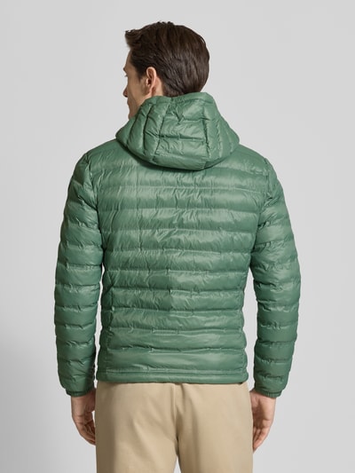 Männermodel trägt grüne Steppjacke mit Kapuze, Zweiwege-Reißverschluss, Label-Detail, Regular Fit, Modell 'Charles' von Blauer Usa, Rückenlänge 65 cm, Schulterbreite 47 cm, Brustweite 55 cm, Ärmellänge 65 cm, Ganzkörperansicht Rückansicht.