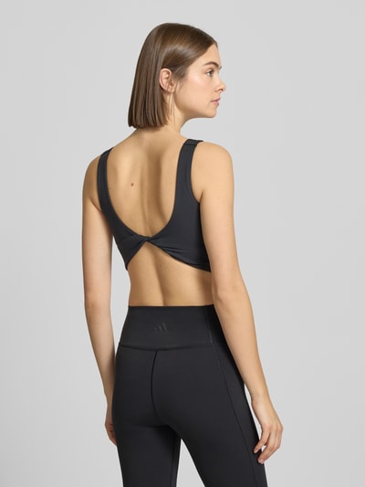 Modelka nosi Crop Top mit Label-Print od adidas Sportswear, czarny elastyczny materiał, krój slim fit, U-dekolt, długość pleców 21 cm, widok z tyłu całej sylwetki.
