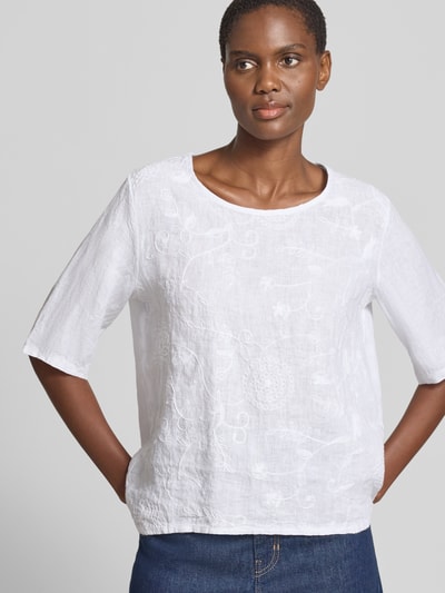 Frauenmodel trägt Regular Fit Leinenbluse mit Stitchings Modell 'Zu44zzi' von ZABAIONE, Rundhalsausschnitt, Reines Leinen, weiße Farbe, glatte Textur, Damen, Rückenlänge 67 cm, Ärmellänge 19 cm, Nahaufnahme Oberkörper.