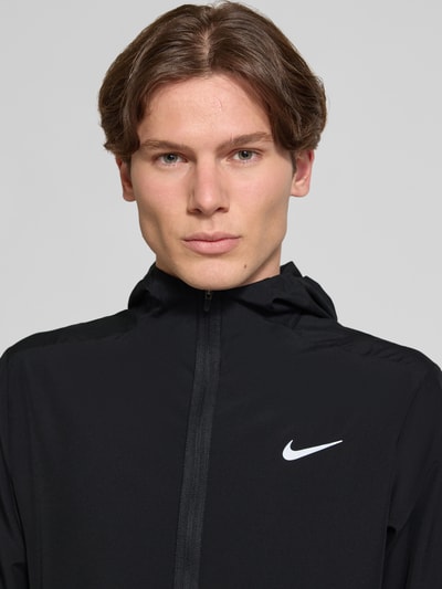 Männermodel trägt schwarze Trainingsjacke mit Logo-Print und Stehkragen von NIKE TRAINING, Reißverschluss, Nahaufnahme Oberkörper.