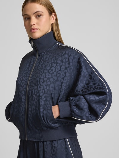 Frauenmodel trägt Tracksuit-Jacke aus Viskose-Mix von Lala Berlin, dunkelblauer Animal-Print, Reißverschluss, Eingrifftaschen, Nahaufnahme Oberkörper.