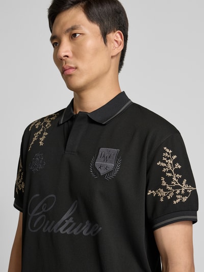 Männermodel trägt Poloshirt floralem Allover-Stitching von Don’t Waste Culture, Schwarz mit beigen Stickereien, Logo-Print, Nahaufnahme Oberkörper.