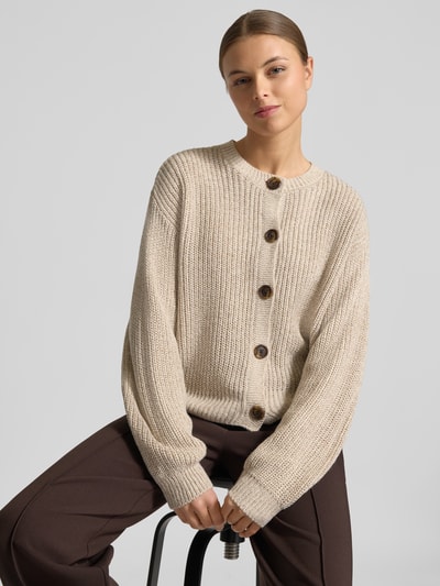 Modelka kobieca nosi Regular Fit Strickjacke mit einreihiger Knopfleiste Modell 'LEA' od Vero Moda, kremowy sweter dzianinowy, długi rękaw, krój regular fit, okrągły dekolt, prążkowane wykończenia, gładka faktura, zdjęcie z przodu, ujęcie do pasa.