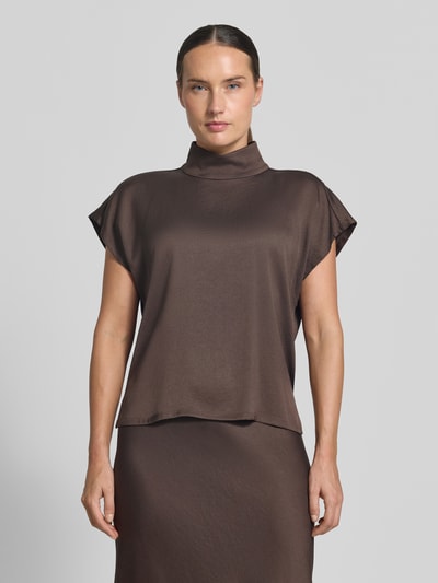 Frauenmodel trägt Blusentop mit Stehkragen Modell 'ALARIA' von DRYKORN, brauner Material-Mix mit Stretch, glatte Struktur, Regular Fit, Ganzkörperansicht von vorne.