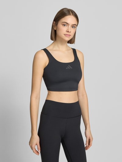 Kobiece model prezentuje Crop Top mit Label-Print od adidas Sportswear, czarny, materiał z domieszką stretchu, krój slim fit, ujęcie całej sylwetki z przodu.
