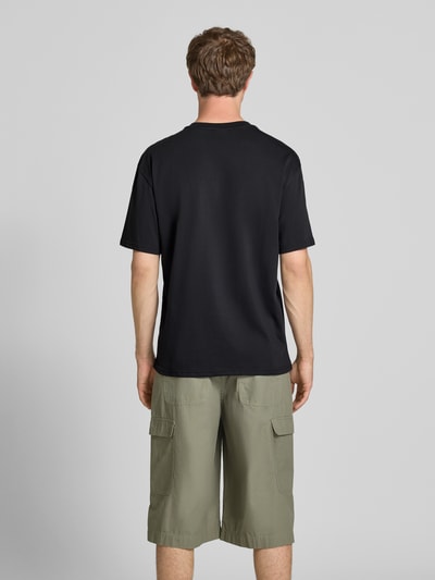 Männermodel trägt Oversized Fit T-Shirt mit Logo-Stitching von KARL KANI aus reiner Baumwolle, Rückansicht, Ganzkörperansicht. Rückenlänge bei Größe M: 72 cm, Rundhalsausschnitt.
