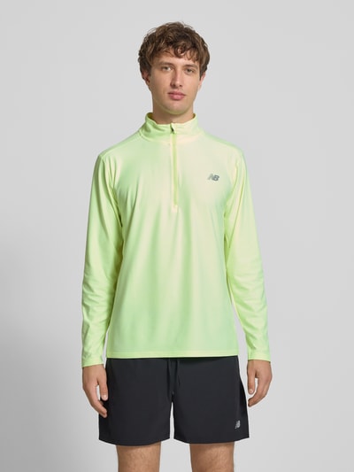 Męski model nosi Regular Fit Sweatshirt mit Troyer-Kragen od New Balance z elastycznej mieszanki materiałów, nadruk z logo, długość tyłu w rozmiarze M: 69 cm, jasny zielony kolor, gładka tekstura, pełen przód, krój regular fit, zdjęcie: całkowity widok od przodu.