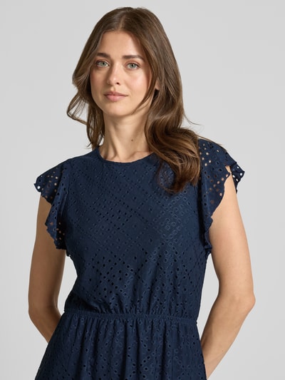 Frauenmodel trägt tailliertes Sommerkleid mit Lochstickmuster Modell 'TASSA' von Vero Moda, unifarben, kurzarm, Nahaufnahme Oberkörper.