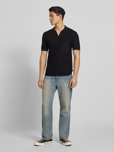 Männermodel trägt Slim Fit Poloshirt in Strick-Optik von Replay in Schwarz, reine Baumwolle, V-Ausschnitt, gerippte Abschlüsse, Ganzkörperansicht von vorne.