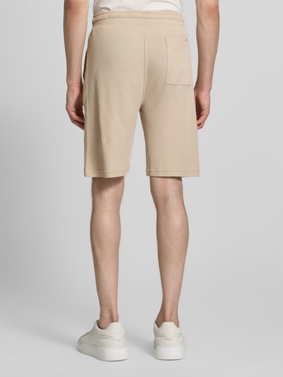 Männermodel trägt Relaxed Fit Sweatshorts aus Baumwoll-Mix von s.Oliver RED LABEL in Beige mit Struktur, Label Patch, Rückansicht Ganzkörperansicht.