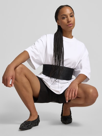 Vrouwenmodel draagt Oversized T-shirt met Label-Patch van black palms, puur katoen, oversized fit, ronde hals, ruglengte maat S 73 cm, effen wit, korte mouwen. Ganzkörperaanzicht van voren.