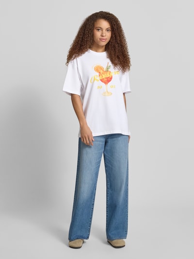 Frauenmodel trägt T-Shirt mit rückseitigem Motiv-Print von REVIEW, Damen T-Shirt aus Reine Baumwolle, Oversized, Rundhalsausschnitt, Vorderansicht, Ganzkörperansicht von vorne.