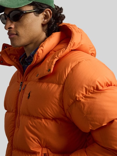 Männermodel trägt Steppjacke mit Zweiwege-Reißverschluss von POLO RALPH LAUREN in Orange, unifarben, Kapuze, Polyester, Nahaufnahme Oberkörper.