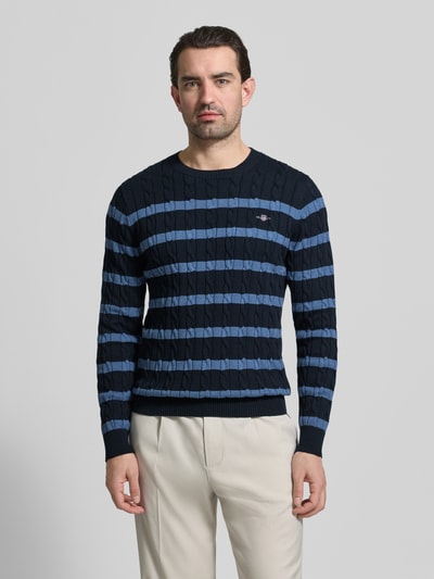 Männermodel trägt Slim Fit Pullover in Strick-Optik von Gant, Baumwolle, Rundhalsausschnitt, Logo, dunkelblau gestreift, Ganzkörperansicht von vorne.