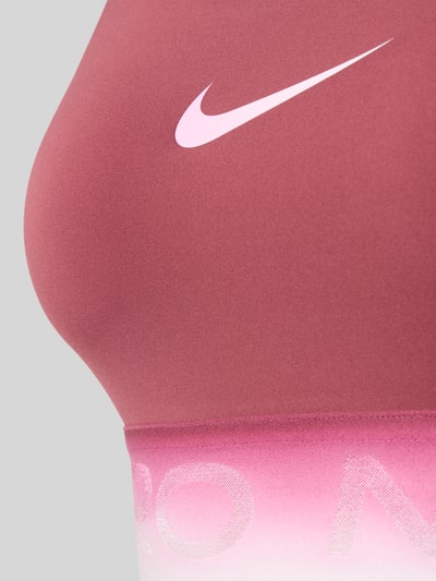 Frauenmodel trägt Sport-BH mit Label-Bund von Nike in Rosa und Pink mit glatter Oberfläche, Nahaufnahme Oberkörper. Damen Sport-BH von Nike.