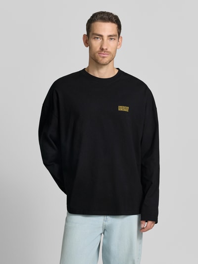 Männermodel trägt schwarzes Longsleeve mit gelbem Logo-Print Modell 'GIXY' von American Vintage, Baumwolle, Rundhalsausschnitt, Ganzkörperansicht von vorne.