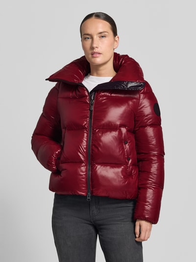 Frauenmodel trägt Regular Fit Steppjacke mit Stehkragen Modell 'Isla' von Save The Duck in glänzendem Dunkelrot, Ganzkörperansicht von vorne.