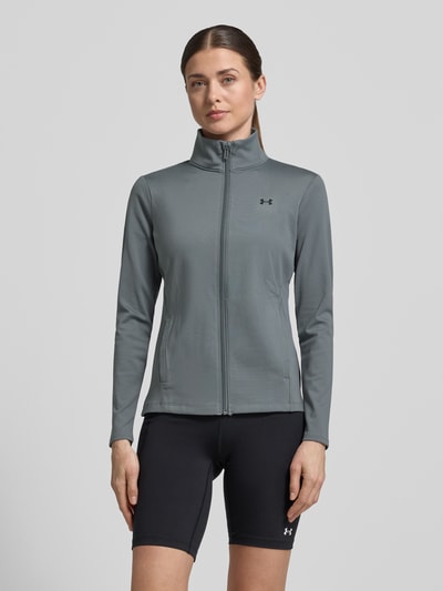 Vrouwenmodel draagt trainingsjack met opstaande kraag en logoprint van Under Armour, materiaalmix met stretch, slim fit, steekzakken, ritssluiting, ruglengte maat S 59 cm, schouderbreedte 35 cm, borstwijdte 43 cm, mouwlengte 60 cm, grijs, glad oppervlak, zwart logo, voorkant, geheel zicht. Ganzkörperansicht von vorne.