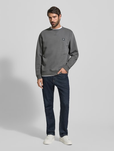 Męski model nosi Sweatshirt mit Rundhalsausschnitt und Label-Patch od Lerros z mieszanki bawełny, krój relaxed fit, okrągły dekolt, długość tyłu 72 cm, długość rękawów 66 cm, kolor szary, tekstura gładka, naszywka z logo, cała sylwetka z przodu.