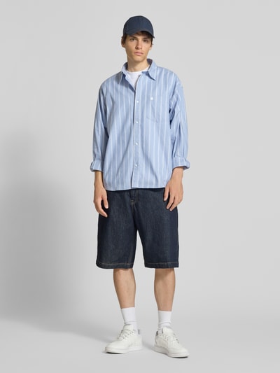 Männermodel trägt Regular Fit Freizeithemd mit Kentkragen und Label-Stitching von Carhartt Work In Progress, hellblau, Ganzkörperansicht von vorne.