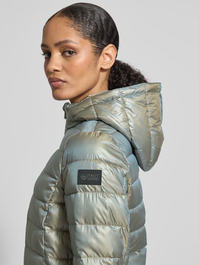 Kobiece model prezentuje Jacke mit Kapuze od NAUTGÅRD, jasnoniebieska, matowa struktura, detal z logo, zbliżenie na górną część ciała, z boku. Długość tyłu w rozmiarze M: 90 cm, szerokość ramion w rozmiarze M: 45 cm, szerokość w klatce piersiowej w rozmiarze M: 56 cm, długość rękawa w rozmiarze M: 60 cm.