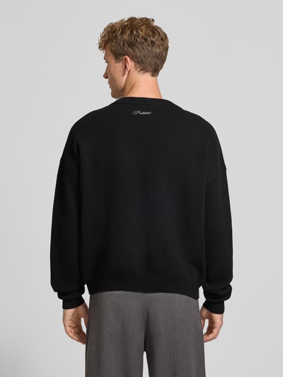 Męskimodel nosi czarny Relaxed Fit Strickpullover aus reiner Baumwolle od PROHIBITED, wyhaftowane logo, prążkowane wykończenia, widok całej sylwetki od tyłu. Długość tyłu w rozmiarze M: 64 cm, długość rękawów: 59 cm, luźny krój, sweter z dzianiny, bawełna.