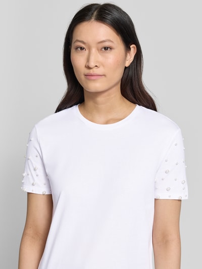 Modelka kobieca nosi t-shirt z okrągłym dekoltem i perłami od Jake*s Casual, bawełna, krój regular fit, długość tyłu w rozmiarze S: 53 cm, biała kolorystyka, prosta faktura, zbliżenie na górną część ciała, widok z przodu.
