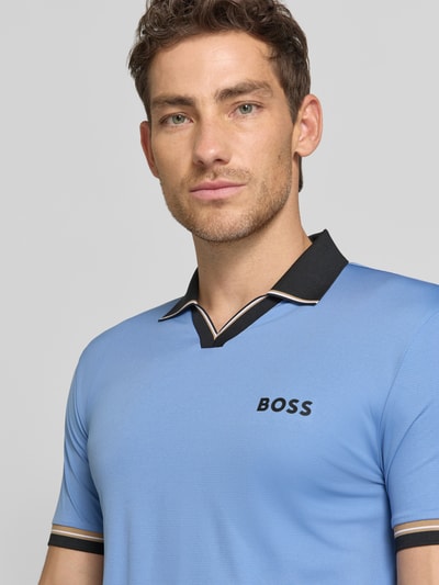 Mężczyzna model nosi Slim Fit Poloshirt mit Label Print Modell 'PL_TOC SERVE 2' von BOSS Green, niebieski kolor, kontrastowe paski, kołnierz polo, krótki rękaw, krój regular fit, detal z nadrukiem logo, zbliżenie na górną część ciała.