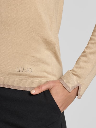 Frauenmodel trägt Slim Fit Longsleeve aus Viskose-Mix mit V-Ausschnitt von Liu Jo White in Beige, Logo-Detail, elastische Abschlüsse, Nahaufnahme Oberkörper.